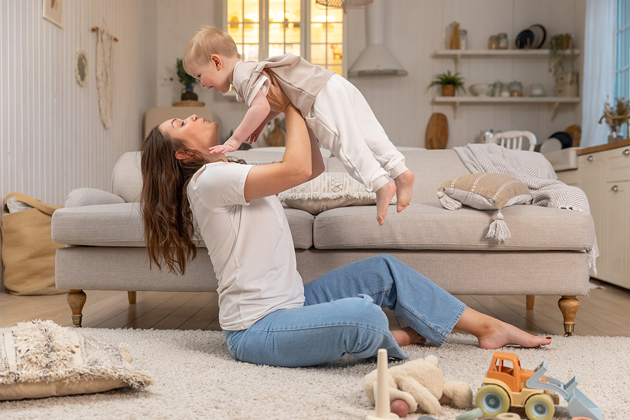 Happy Family At Home. Mother Lifting In Air Little Toddler Child