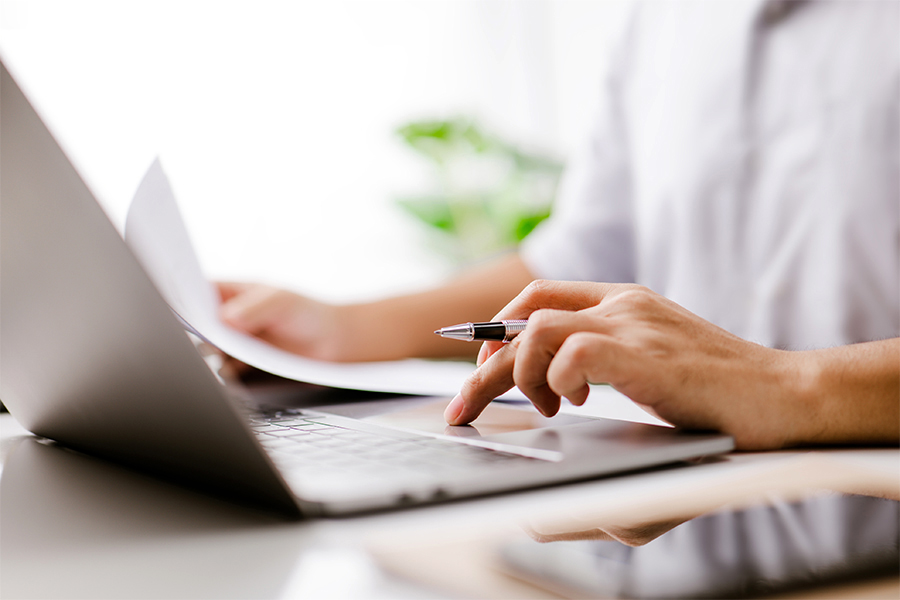 Businessman hand is on the trackpad, typing on a laptop keyboard, while reading a business document. In a modern office, a corporate man, a lawyer, works. Concept of business and technology.
